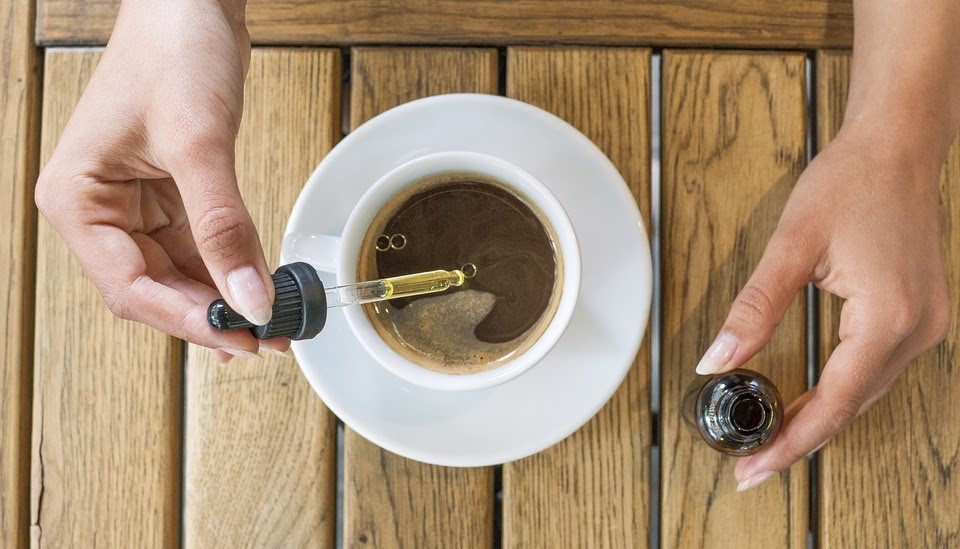 hands adding cbd droplets to coffee